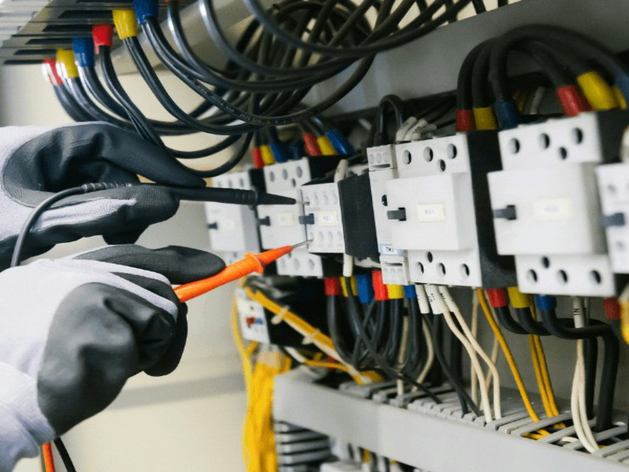 Gloved hand holding a test probe against industrial contactors